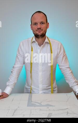 Vertical shot of a handsome tailor working on a suit jacket pattern in an atelier in France. Stock Photo