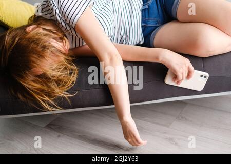 Young woman fall asleep after long using of smart phone on the sofa in the living room. Bad influence of social web sites Stock Photo
