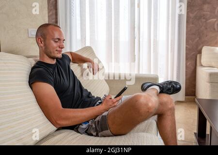 Beautiful young man relaxing on sofa and looking at his smart phone. Technology concept Stock Photo