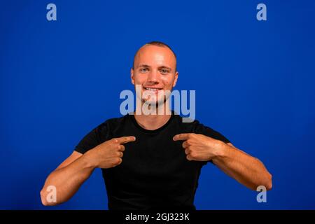 Extremely surprised teenager in black casual style hoodie pointing fingers on himself with widely opened mouth and eyes, shocked with victory Stock Photo