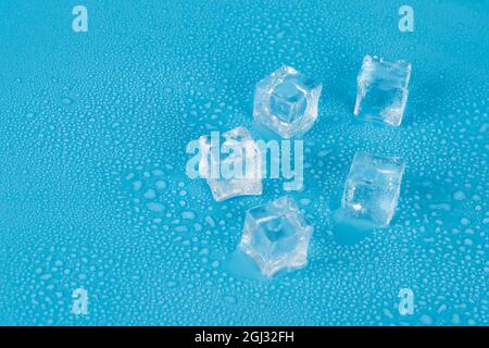 Five ice cubes lie on a blue background in water droplets. Free space. Cubes are located on the right side of the picture Stock Photo