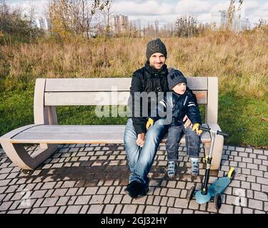 POZNAN, POLAND - Nov 12, 2017: A man and a boy sitting on a wooden bench at a park. Stock Photo