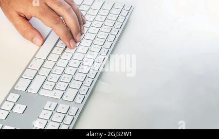 a male hand typing on a modern computer keyboard. Work and employment. Copy space. Wireless technology Stock Photo