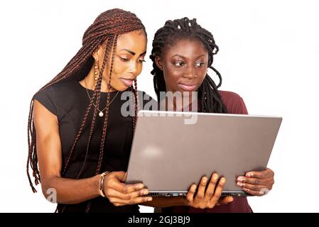 two young beautiful sisters standing in black and red colors holding and using a laptop while smiling Stock Photo