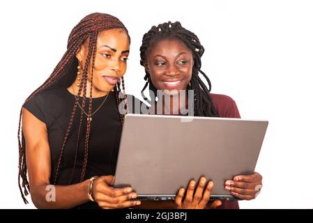 two young beautiful sisters standing in black and red colors holding and using a laptop while smiling Stock Photo