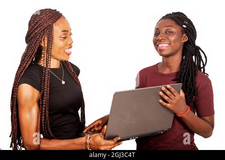 two smiling beautiful sisters standing in burgundy black and red colors holding and using a laptop Stock Photo