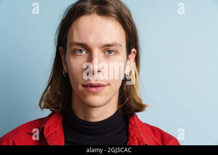 Young white man wearing red jacket posing and looking at camera isolated over blue wall Stock Photo