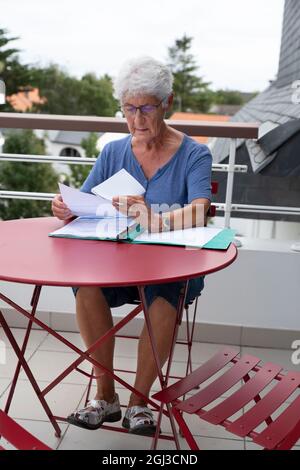 An elderly woman reads written administrative documents sitting at a table Stock Photo