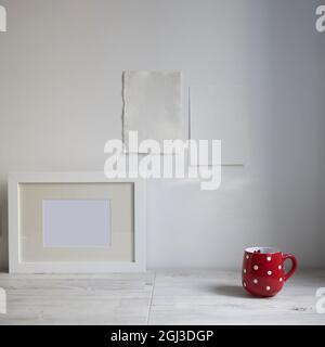 Scandinavian style. Interior Design. A red cup in the dot, a frame for a photo are on the table. Two blank sheets of paper are attached to the wall. E Stock Photo