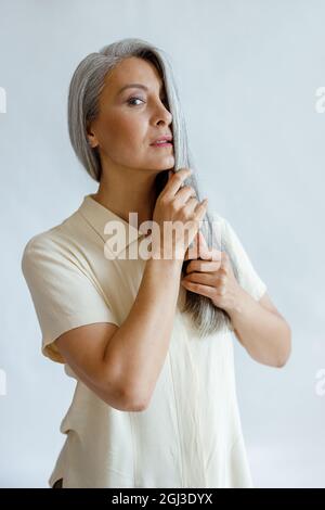 Attractive mature Asian model in hides half of face with silver hair on light background Stock Photo
