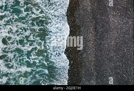Sea waves breaking on wild beach with black sand and pebbles, aerial natural background Stock Photo