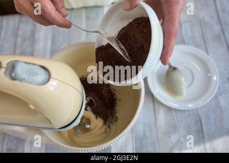 Cake making process. Female hands add cocoa to the mixer bowl for making dough. Step by step recipe for chocolate cake. Series. Baking concept. Stock Photo