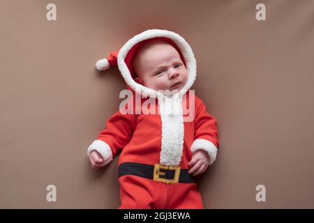 Newborn girl dressed in santa claus costume looking at camera with confused face. Stock Photo