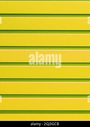 Yellow metal fence made of corrugated steel sheet with vertical rails. Corrugated yellow with light green stripes iron sheet close up background. Stock Photo