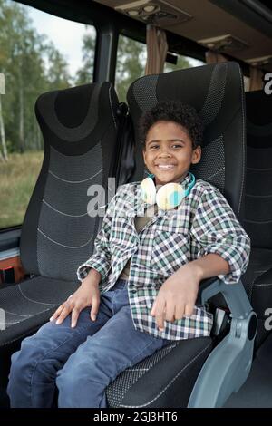 Portrait of happy black boy with curly hair sitting in bus seat and riding bus alone Stock Photo