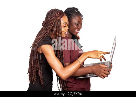 Two young beautiful girlfriends standing perplexed in black and red clothes holding, using a laptop and smiling isolated on white background Stock Photo