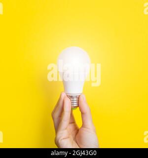 Hand holding a LED light bulb on bright yellow background. Using economical and environmentally friendly light bulb concept. Idea concept. Energy Stock Photo