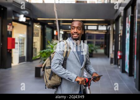 African businessman with his electric scooter. Smiling guy elegantly dressed goes to work with a non-polluting vehicle - Clean mobility concept Stock Photo
