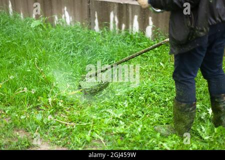 Mows the grass with a hand-held lawn mower. The gardener is cutting the lawn. The gardener's tool cuts tall grass. The lawn mower in action. Stock Photo