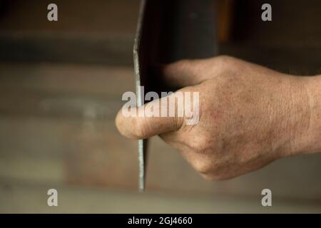 Worker with metal. The guy holds a steel part. Hard work in a metalworking workshop. Creation of steel construction. The working hands of a man. Stock Photo