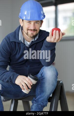 handsome young construction worker eating red apple on site Stock Photo