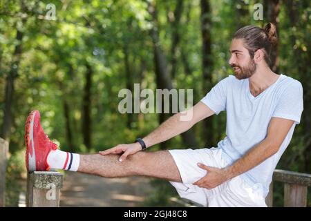 young fit man stretching legs outdoors doing forward lunge Stock Photo