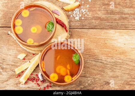 Transparent chicken broth with vegetables in ceramic bowls. Traditional bouillon, healthy food, cutlery. Old wooden background, top view Stock Photo