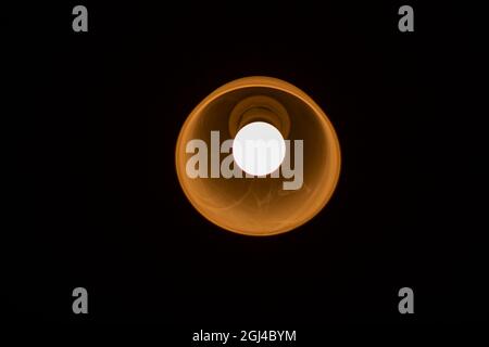 The lamp shines in the dark. Round light source. Warm glow from the room lamp. Stock Photo