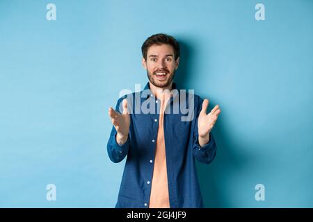 Cheerful young man pointing hands at camera and smiling, feeling glad for you, praising nice work, standing on blue background Stock Photo