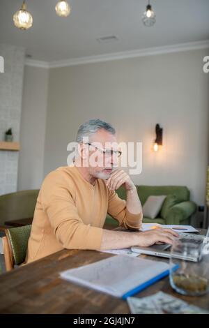 Gray-haired man working on a laptop and looking busy Stock Photo