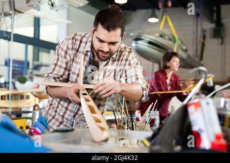 Young handsome bearded man enjoying his hobby - modeling light airplanes in aircraft hangar Stock Photo