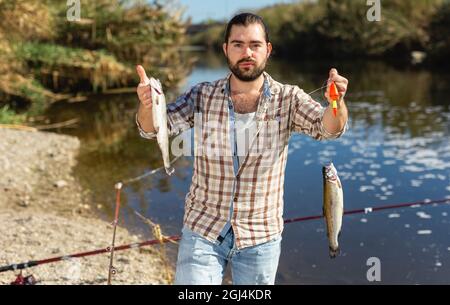 Premium Photo  Serious fisher male holding casting rod standing on bank  waiting for bites on water river at cloudy summer day looking at camera