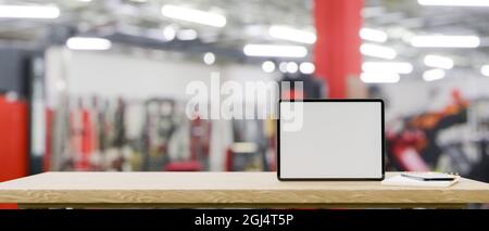 Mockup space on wooden tabletop with blank screen tablet mockup over blurred fitness gym in the background, Technology and sport concept, 3d rendering