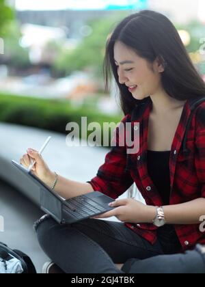 Young female freelancer working digital tablet with stylus pen at city park, college student relaxing at park in sunny day with tablet Stock Photo