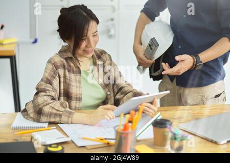 Two architects in office discussing layout of building together on digital tablet , A young female architects working with male engineers in office Stock Photo
