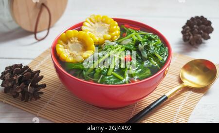 Known well as Sayur bening bayam or spinach clear soup is Indonesian food made from spinach, carrot, corn, and other vegetables. Served on red bowl on Stock Photo