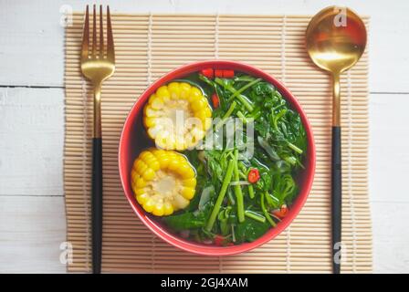 Known well as Sayur bening bayam or spinach clear soup is Indonesian food made from spinach, carrot, corn, and other vegetables. Served on red bowl on Stock Photo