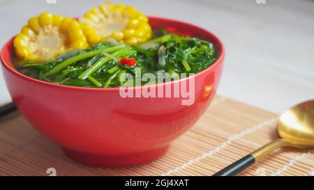 Known well as Sayur bening bayam or spinach clear soup is Indonesian food made from spinach, carrot, corn, and other vegetables. Served on red bowl on Stock Photo