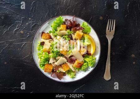 Chicken Caesar salad, shot from the top on a black background. Romaine leaves, crispy croutons, chicken meat, and the classic dressing Stock Photo