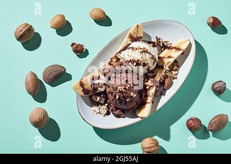 Top view of appetizing banana split dessert with vanilla and chocolate balls of ice cream garnished with syrup and hazelnuts served on light blue back Stock Photo