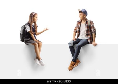Schoolgirl and a teenage boy student sitting on a blank board and talking isolated on white background Stock Photo