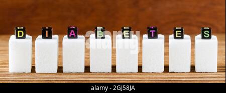 Inscription DIABETES from small toy cubes on the white sugar cubes. Brown wooden background, closeup, selective focus Stock Photo
