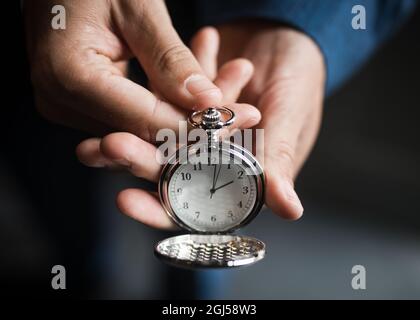 Selective focus on beautiful old retro classic silver pocket watch clock face showing 2 o'clock time held out with cover open on elegant timepiece. Stock Photo