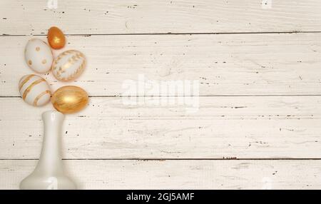 Golden Easter eggs and white vase on rustic old wooden background. Trendy Easter flat lay composition. Copy space for text. Minimal Easter concept. Ea Stock Photo