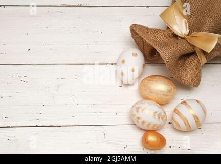 Golden Easter eggs in jute bag on rustic old wooden background. Trendy Easter flat lay composition. Copy space for text. Minimal Easter concept. Happy Stock Photo