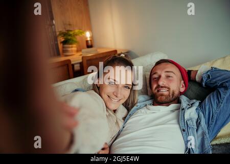Happy caucasian couple sitting on sofa taking selife Stock Photo