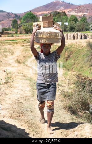 Africa, Madagascar, Antananarivo Province. A woman carrying a large number of bricks on her head. Stock Photo