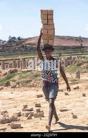 Africa, Madagascar, Antananarivo Province. Brick making factory, a young Malagasy girl carrying dried bricks on her head to where they will be fired. Stock Photo