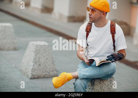 Young disabled man writes in notebook with pen in artificial prosthetic hand at city street outdoors urban Stock Photo