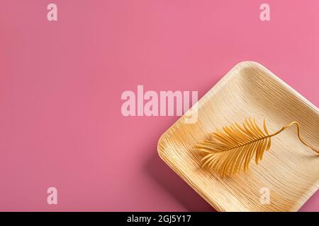 Dry curved plant leaf of golden yellow color on a textured square plate of palm leaf against pastel pink background. Yellow pink blank message card. Stock Photo